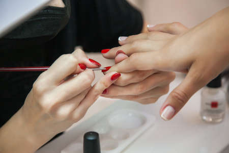 Gel polish design. Female master in the salon is painting with brush on the hands of the client. Beauty industry, creativity concept.の写真素材