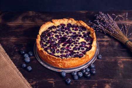 Rustic shortbread pie with blueberries in sour cream filling on a wooden background and a bouquet of dried lavenderの写真素材