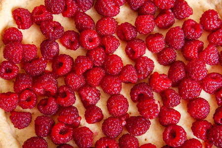 Background of raspberries lying on Shortcake dough, top view close up.