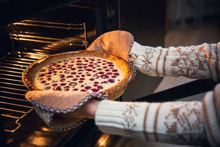 Woman in Christmas sweater takes raspberry shortcake out of the oven.の写真素材