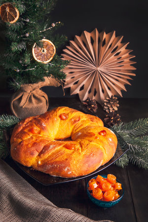 Home baked Christmas bread in a shape of Advent wreath of yeast dough with orange candied fruits on background of Christmas tree.の写真素材