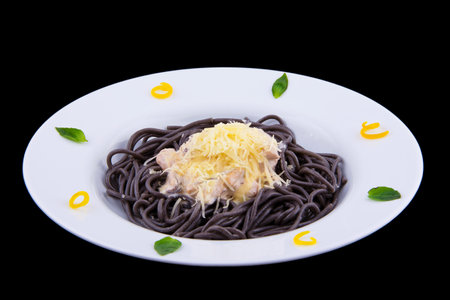 Black spaghetti with seafood in white sauce and cheese on a white plate on black background.の写真素材
