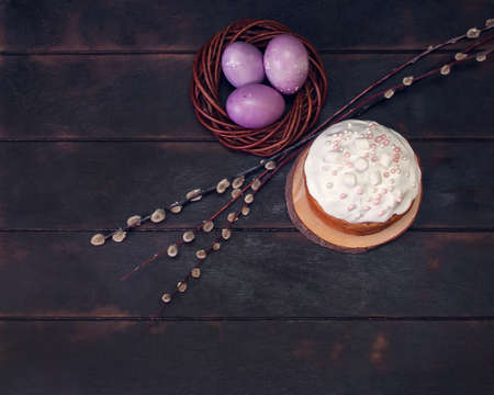 Easter cakes on a dark background, decorated with marshmallows and painted Easter eggs in a wicker...
