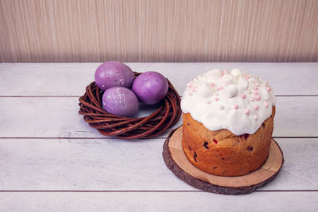 Easter cakes decorated marshmallows, and painted Easter eggs in a wicker nest on a light wooden...