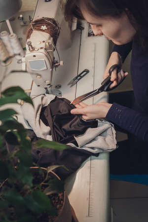 Seamstress sews clothes and cuts the seam on a fashionable jacket made of velvet fabric, on a sewing machine in her studio, top viewの写真素材
