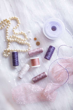 Items for tailoring - spools of thread, needles, ribbons, lace, buttons, pearl necklace on a background of tulle with sequinsの写真素材