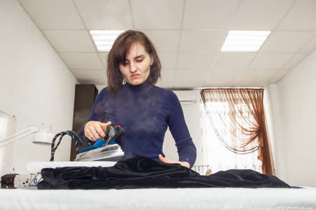 Seamstress steams a velvet jacket with an iron in her atelier. Authentic lifestyle.の写真素材