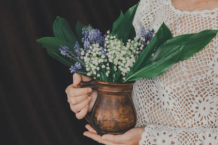 Bouquet of lilies of the valley in ceramic jug in the hands of woman in knitted blouse.の写真素材