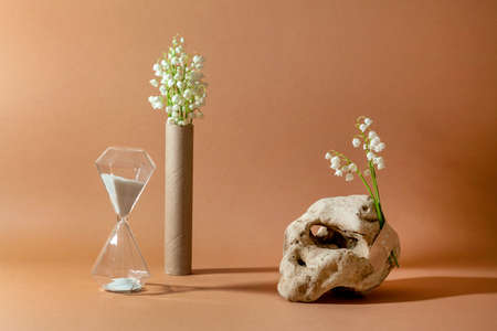 Modern still life with unusual natural stone, with bouquet of lilies of the valley and hourglass....