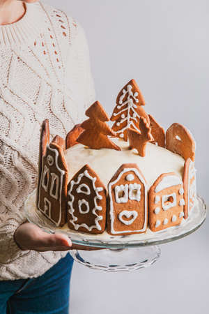 Woman holds homemade cake with gingerbread city house facades, a Christmas tree and reindeer on glass standの写真素材