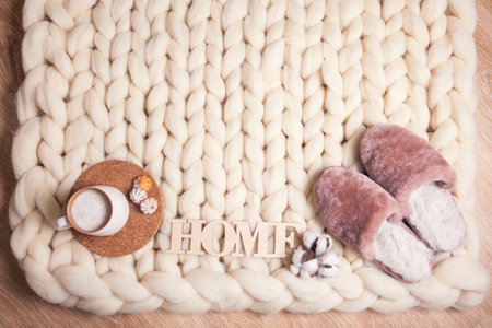 Home slippers made of fur, cup of cappuccino and inscription Home on the background of blanket of thick yarn with copy space.の写真素材