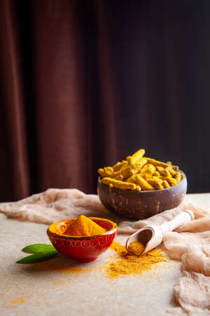 Dried turmeric powder with leaves and roots in coconut shell bowl.
