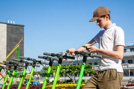 A young man rents an electric scooter by scanning the QR code with a smartphone. Kick scooters in...