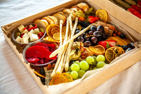 Delicious wine snacks in a cardboard box for a buffet for a party: cheeses, sausages, cold cuts,...
