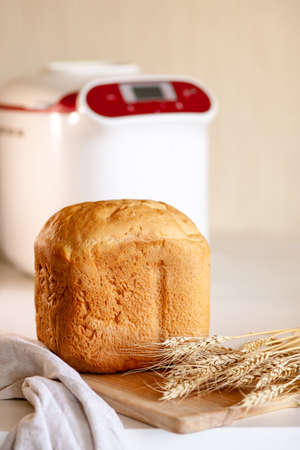 Bread from a bread maker with wheat spikelets on a board with a kitchen napkin.の写真素材