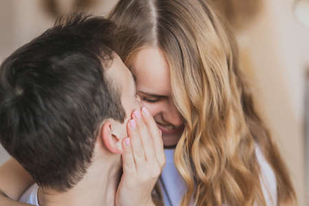 Close up defocused portrait of young attractive romantic couple hugging and kissing, laying down on a bed, being loving with each other. Love and relationships lifestyle, interior bedroom.の写真素材