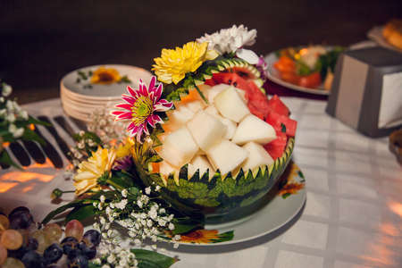 Carved watermelon filled with pieces of melon and watermelon pulp, decorated with fresh flowers.の写真素材