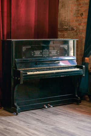 Old vintage piano stands in the hall against the background of a red curtain and a brick wall.の写真素材