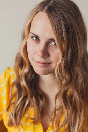 Portrait of beautiful smiling young blonde woman with long curly hair in retro yellow dress, looking...