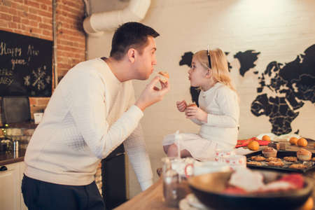Father and daughter play, cook and eat Christmas cookies and muffins in the loft-style kitchen.の写真素材