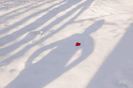 The shadow of a man lies on the snow, a red heart lies in the chest area in sunny winter evening on...