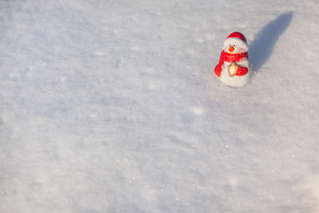The snowman toy stands on the snow cover in sunny winter evening on sunset. Minimalistic snow background with snowman with copy spaceの写真素材