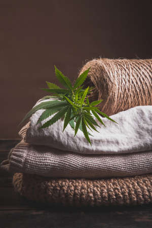 A stack of various types of hemp fiber fabrics. Hemp threads, yarn and fabric with cannabis leaves on a wooden background.の写真素材