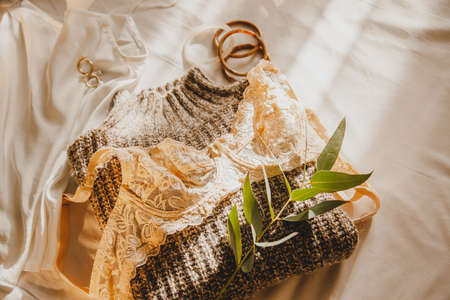 Womens winter wardrobe: lace bra, silk top, coarse knit sweater and accessories lie on a crumpled sheet in the morning sun.の写真素材