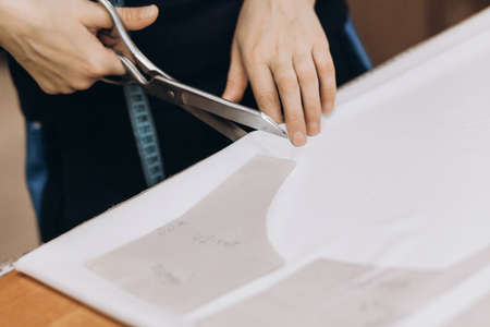 The tailor cuts out the fabric according to the pattern, close up. fabric cutting. Profession of...