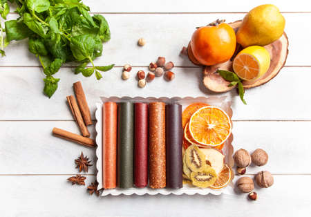 Fruit pastille of different flavors and fruit chips or dried fruit slices in a gift box surrounded by fresh fruits, nuts and spices and fresh basil leavesの写真素材