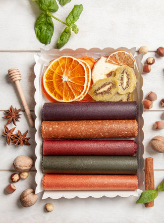 Fruit pastille of different flavors and fruit chips or dried fruit slices in a gift box surrounded by fresh fruits, nuts and spices and fresh basil leavesの写真素材