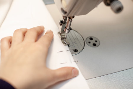 Hands of a dressmaker sewing clothes from white fabric on a sewing machine, close-up.