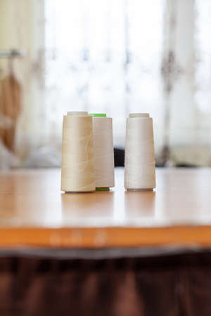 Reels with white threads for a sewing machine on a polished wooden table in atelier