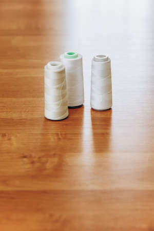Reels with white threads for a sewing machine on a polished wooden table in atelier