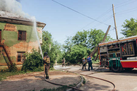 Russia, Rostov-on-Don - June 2, 2022: Firefighter extinguish a fire in an abandoned house with a...