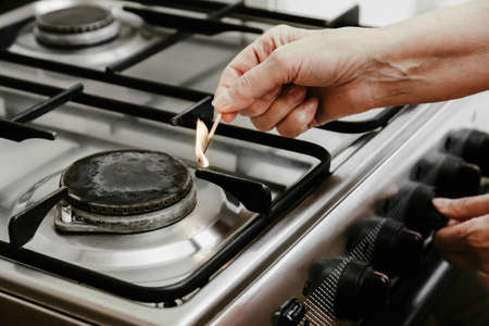 The hand of an adult woman with a matchstick ignites a gas burner or gas-stove in her apartment.の写真素材