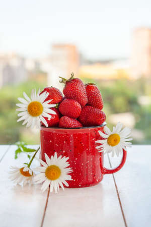 A red mug filled with strawberries and daisies on a light wooden background.の写真素材