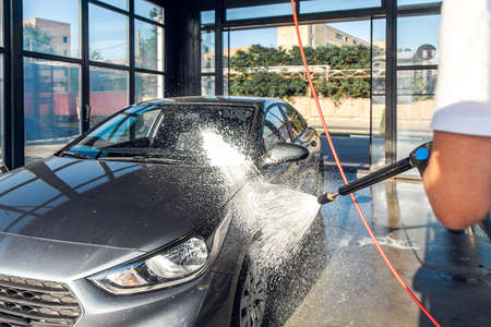 Self service car wash. A man waters his car with foam from a pressurized hose.