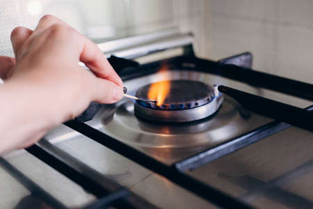 A womans hand with matchstick lights gas stove in her apartment.の写真素材
