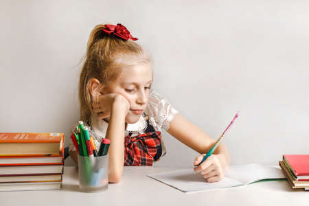 A little girl in a school uniform draws in a notebook with her left hand.の写真素材