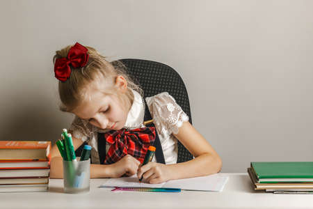 A little girl in a school uniform draws in a notebook with her left hand.