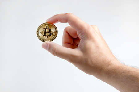 A man's hand holds a gold bitcoin, isolated on a white background.の写真素材
