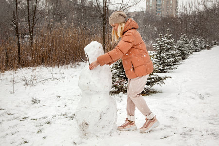 Woman makes a snowman in a city park during a snowfall.の写真素材