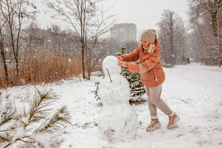 Woman makes a snowman in a city park during a snowfall.の写真素材