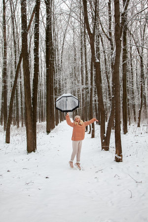 A young woman jumps in a pine forest with a transparent umbrella, trying to take off, rejoicing in winter.の写真素材