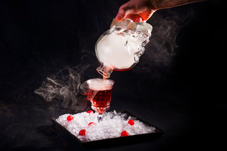 The bartender pours an alcoholic smoky cocktail from a bottle in the form of a skull, the author's serving on a plate with crushed ice and cherries.の写真素材