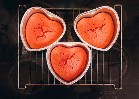 Three red cakes in heart shaped cake pan are on the hob at home. Preparing for Valentine's Dayの写真素材