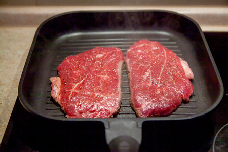Raw minute steak of marbled beef in a grill pan on an electric cooking surface.の写真素材