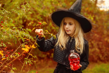 A little witch collects wild berries for a potion, holds a bottle in the form of a skull with a red liquid in her hands.の写真素材