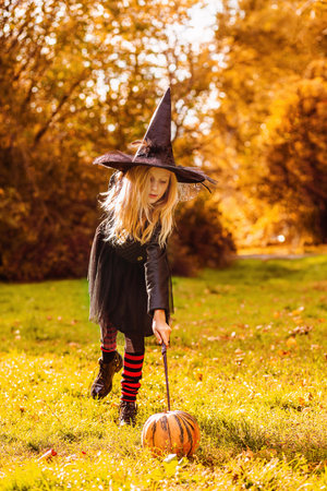 A girl in a witch costume says a spell and enchants a pumpkin with a magic wand.の写真素材